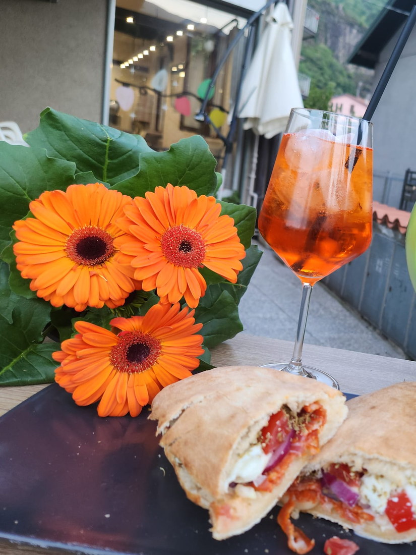 Spritz e pane farcito serviti sul dehors, accanto ai fiori arancioni