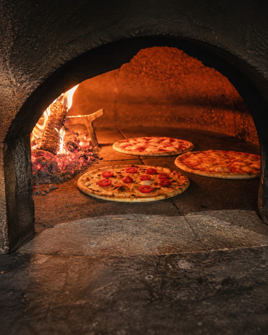 Le pizze nel forno a legna, con la fiamma viva