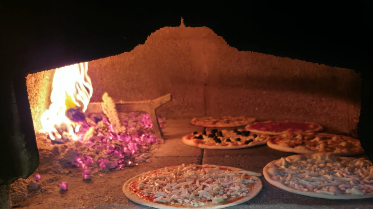 Le pizze in cottura nel forno a legna, con la fiamma e la brace di lato