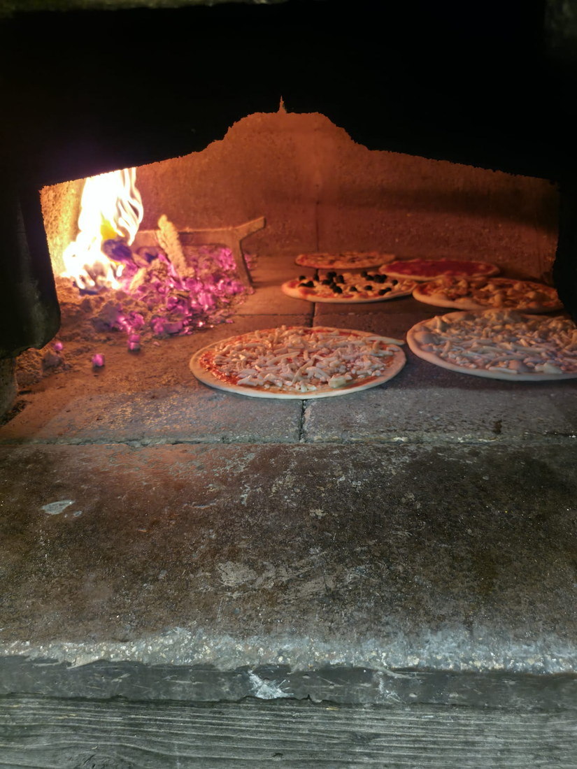 Le pizze nel forno a legna accanto alla fiamma viva e alla brace