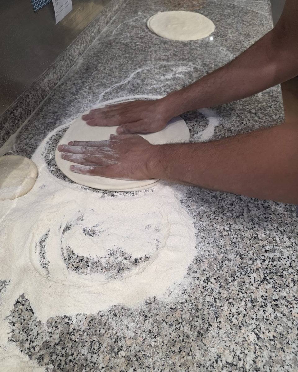 Le mani del pizzaiolo che stendono l'impasto sul bancone di granito infarinato