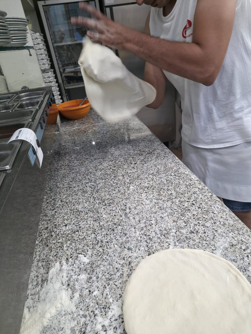 Il pizzaiolo che lancia e allarga l'impasto sopra il bancone