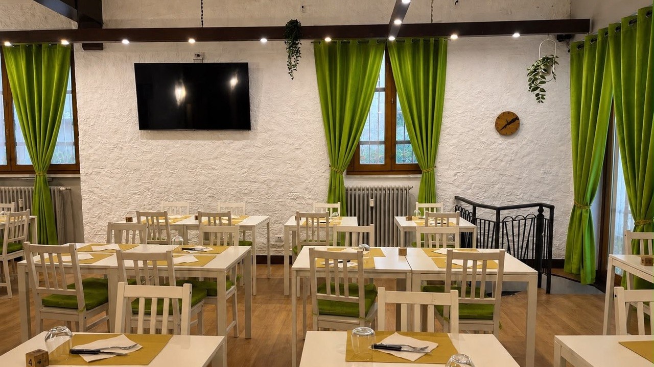 La sala interna con tende verdi, tavoli bianchi e muri in pietra a vista
