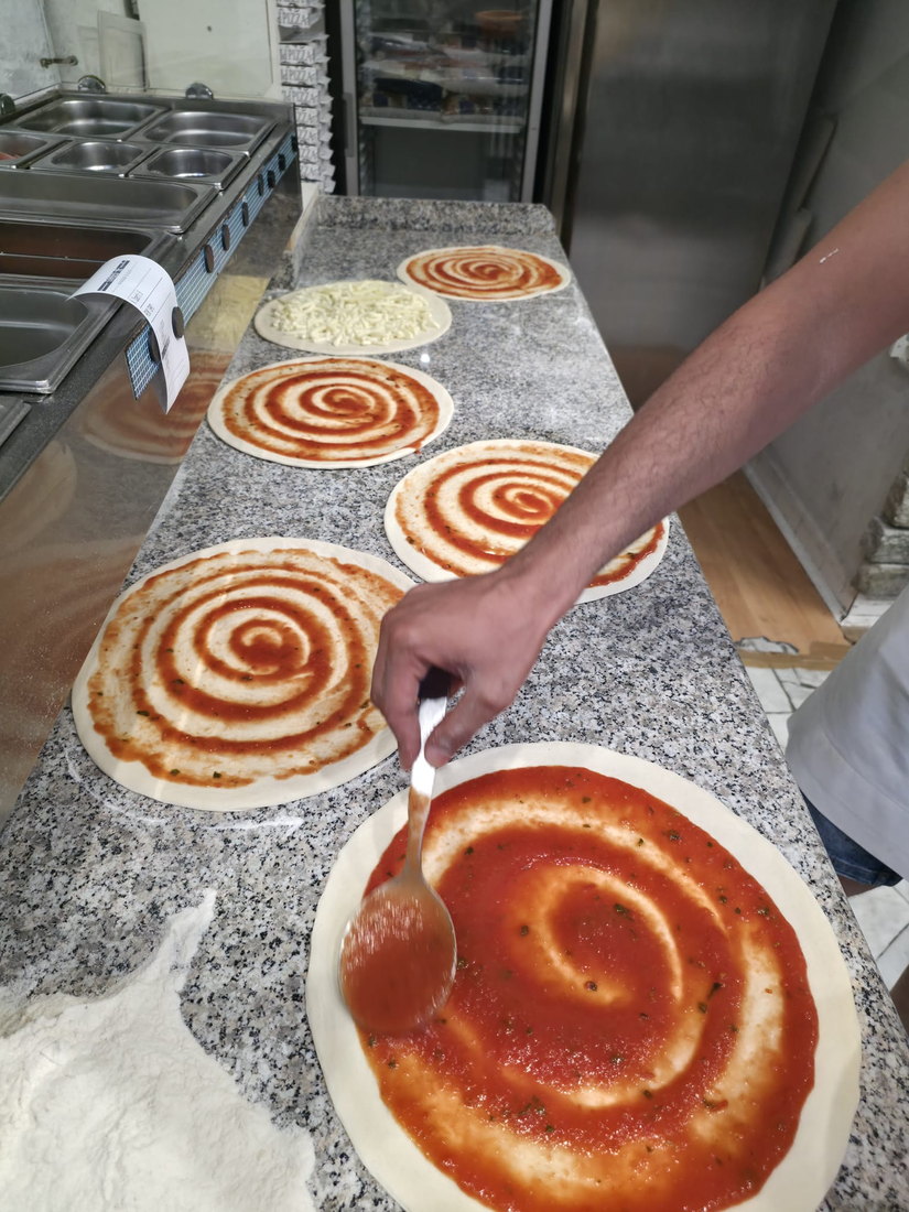 Il cucchiaio che stende la passata di pomodoro a spirale sull'impasto
