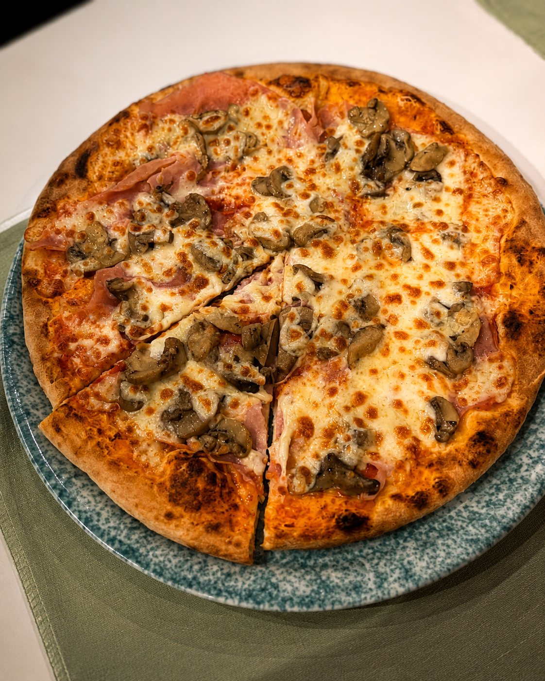 Pizza prosciutto e funghi servita su piatto verde