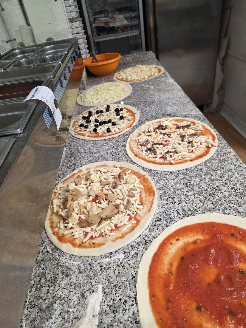 Pizze appena condite allineate sul bancone, pronte per il forno